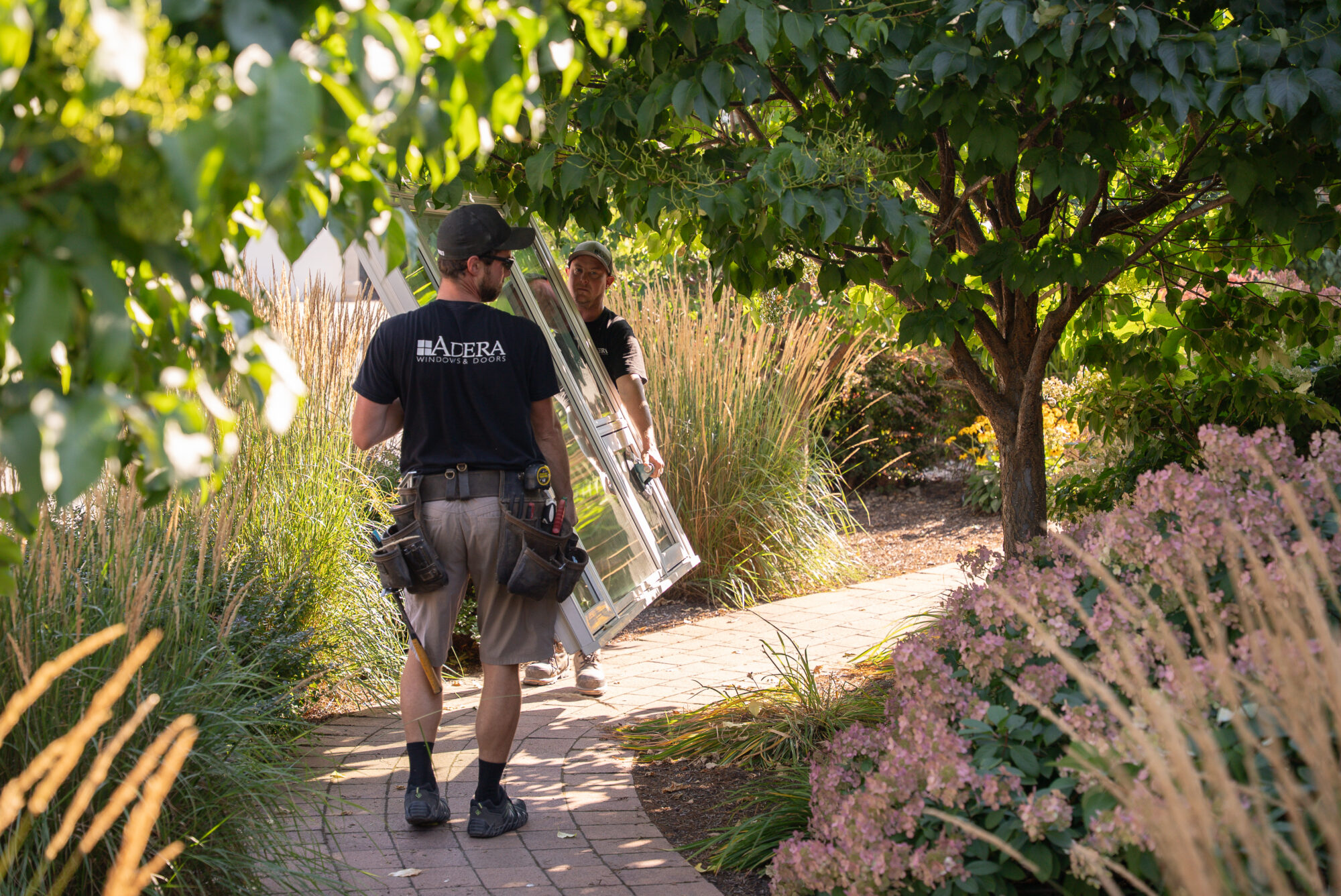 Two men carry a window down a path.